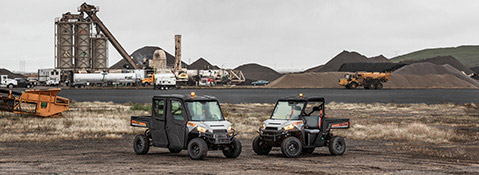 Dos Polaris Commercial XD Full-Size Diesel estacionados en una zona industrial, uno con cabina cerrada y otro con cabina abierta.