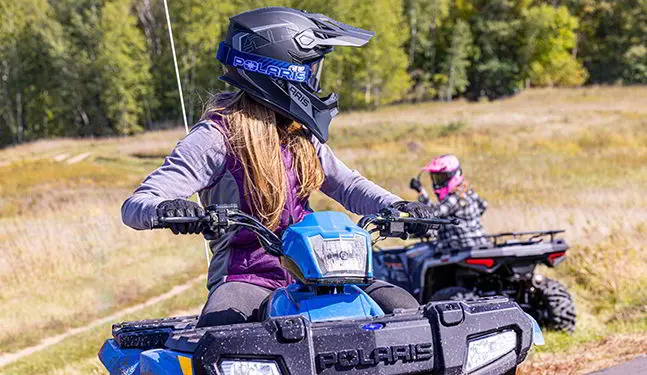 Fille regardant un autre conducteur tout en étant assise dans son VTT pour jeunes Polaris Sportsman 110 2025.
