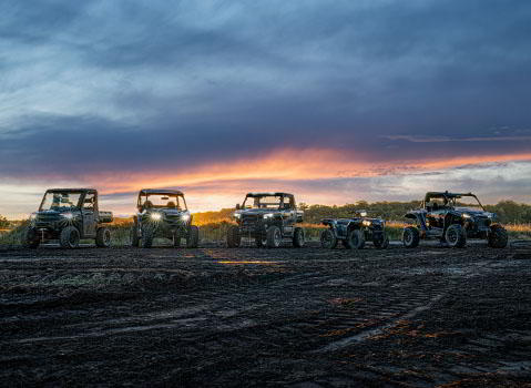 Toda la familia de vehículos Polaris Off-Road alineada ante el cielo del atardecer, mostrando diferentes diseños y características del terreno accidentado.