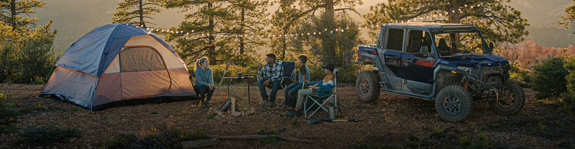 Campers with a Polaris XPEDITION around a campfire.