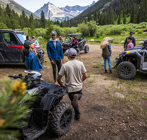 Amigos reunidos alrededor de Polaris ATV y UTV en un campamento de montaña.