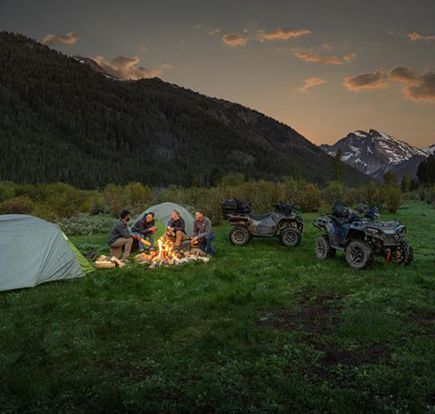 Familia acampando por la noche con Polaris ATV cerca de una fogata y tiendas de campaña.