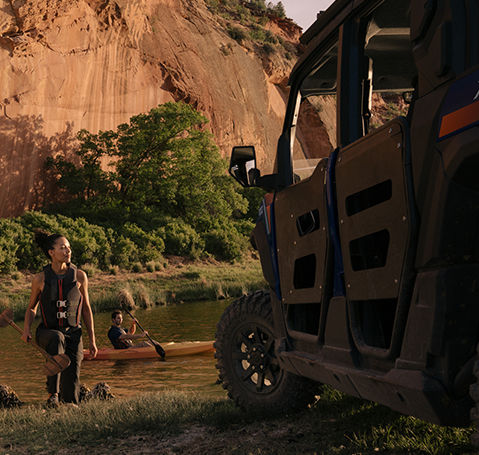 Mujer preparándose para andar en kayak cerca de un UTV Polaris XPEDITION en una ribera.