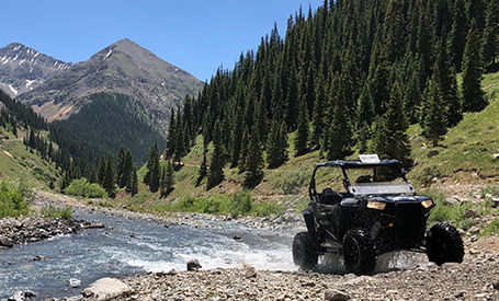 Polaris RZR Trail S conduciendo a través de un río rocoso de montaña.
