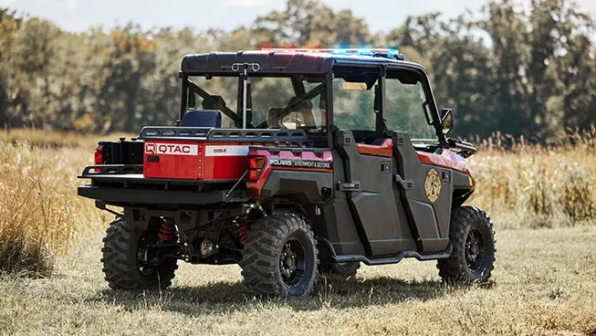 Rear view of a red and black Polaris Government & Defense UTV, modified for EMS response with emergency lights and a Q-TAC EMS module, parked in a grassy field.