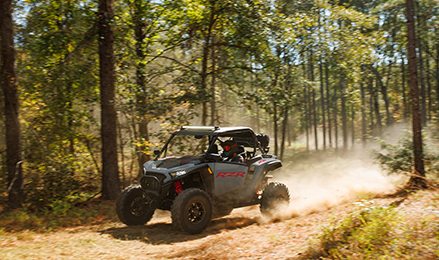 A Polaris RZR XP driving fast through a dense forest.