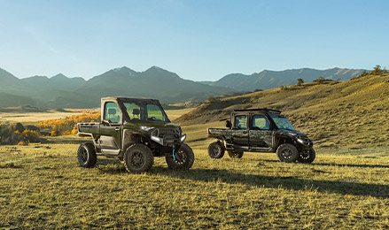 Two Polaris RANGER XD 1500 NorthStar Models, a 2-seat and a CREW 4-seat vehicles, are parked on a grassy field with mountains and a clear sky in the background.