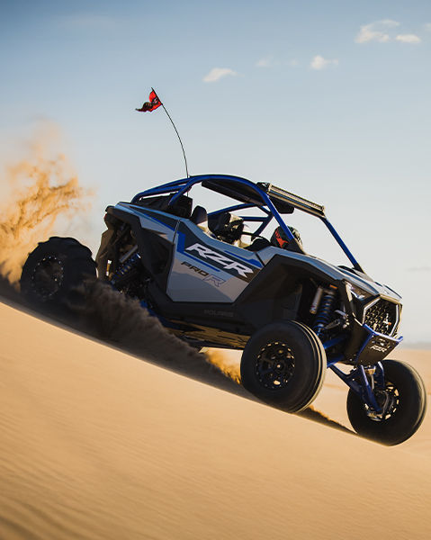 A RZR Pro R descending through a dune with a clear sky in the horizon.