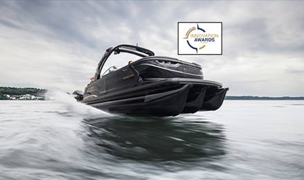 A sleek black Godfrey Sanpan Pontoon boat cruising on a lake, featuring an Innovation Awards logo.