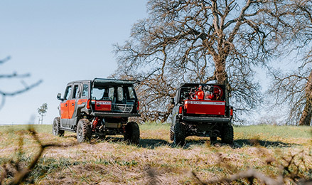 Two Polaris Government and Defense off-road vehicles parked on a grassy field, shown front and rear, with mounted equipment and leafless trees under a clear sky.