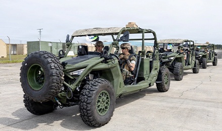 Two Polaris RANGER CREW UTVs equipped with QTAC firefighting units parked in a grassy field beneath large leafless trees on a clear day.