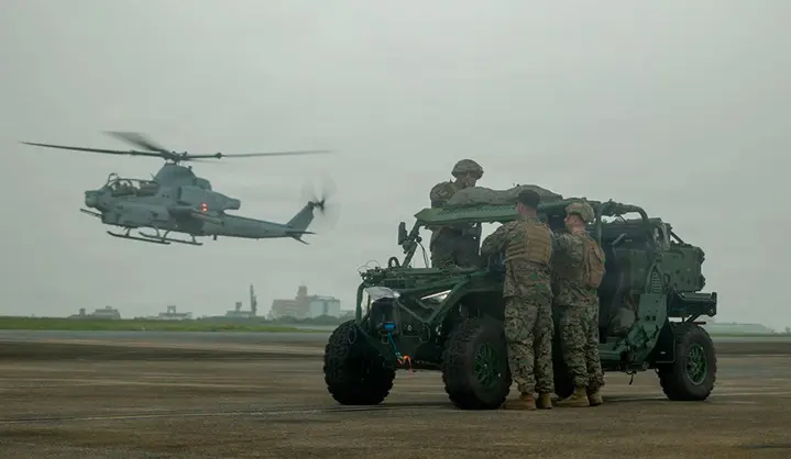 Two Polaris MRZR military Side-by-Side vehicles driving along a muddy jungle trail with headlights illuminated and tactical equipment mounted on the frames.