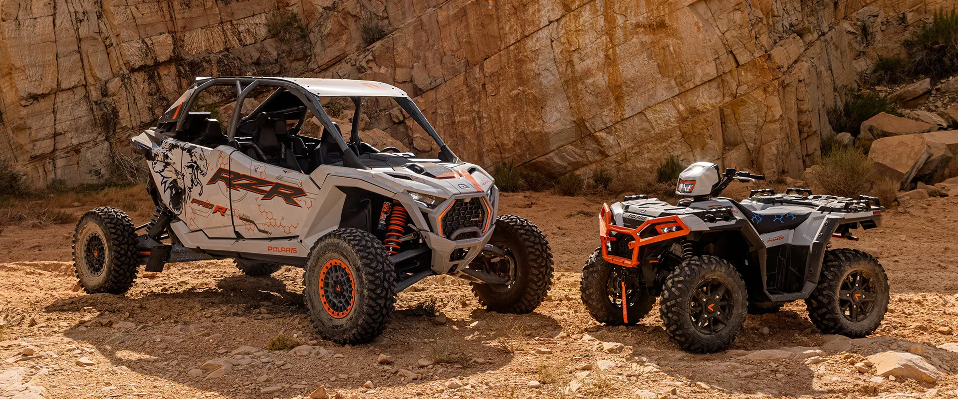 A white and grey Polaris RZR Pro R 4 SxS and a Polaris Sportsman XP 1000 ATV are parked side-by-side in a rocky desert landscape.