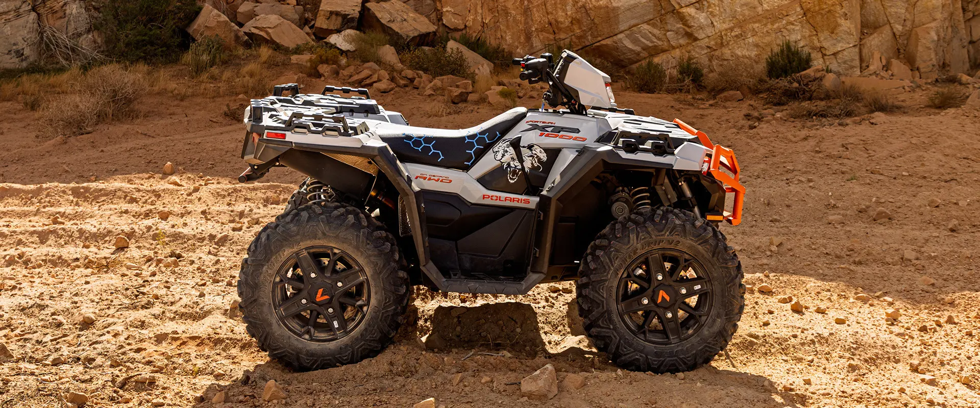 A white and grey Polaris Sportsman XP 1000 ATV is parked on a rocky desert trail.