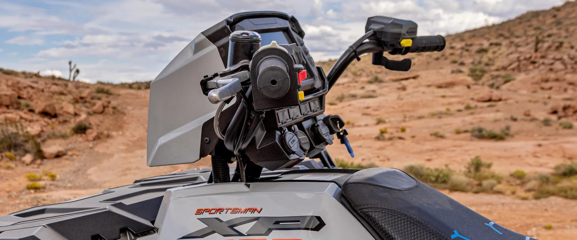 A close-up of the handlebars and front rack of a white and grey Polaris Sportsman XP 1000 ATV in a desert setting.