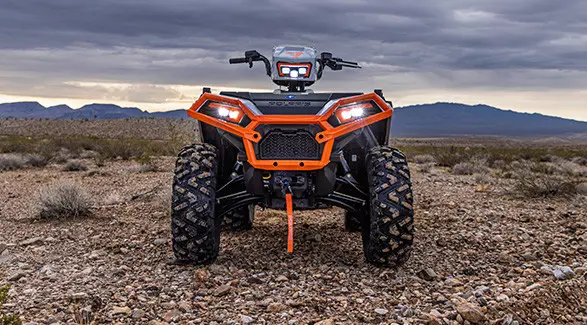 A front view of an orange and grey Polaris Sportsman XP 1000 ATV parked in a desert landscape under a dramatic sky.