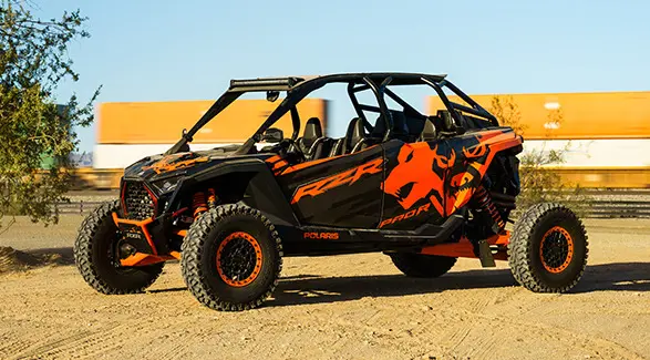 Côte à côte Polaris RZR Pro R 2025 noir et orange stationné sur un sol de terre avec une verdure clairsemée.