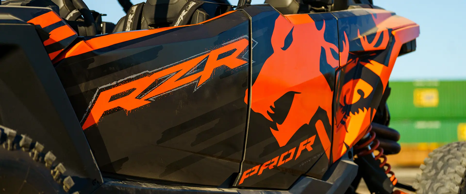 Gros plan sur un véhicule côte à côte Polaris RZR Pro R 2025 avec des motifs orange et noirs audacieux, y compris le logo RZR et des flammes.