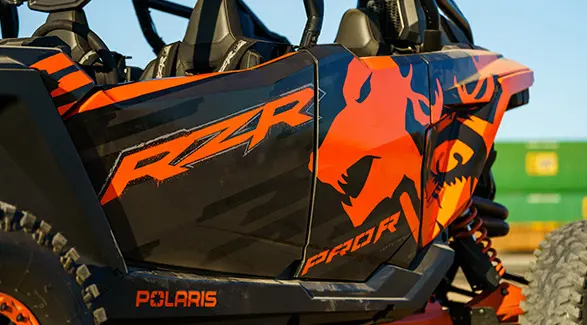 Gros plan sur un véhicule côte à côte Polaris RZR Pro R 2025 avec des motifs orange et noirs audacieux, y compris le logo RZR et des flammes.