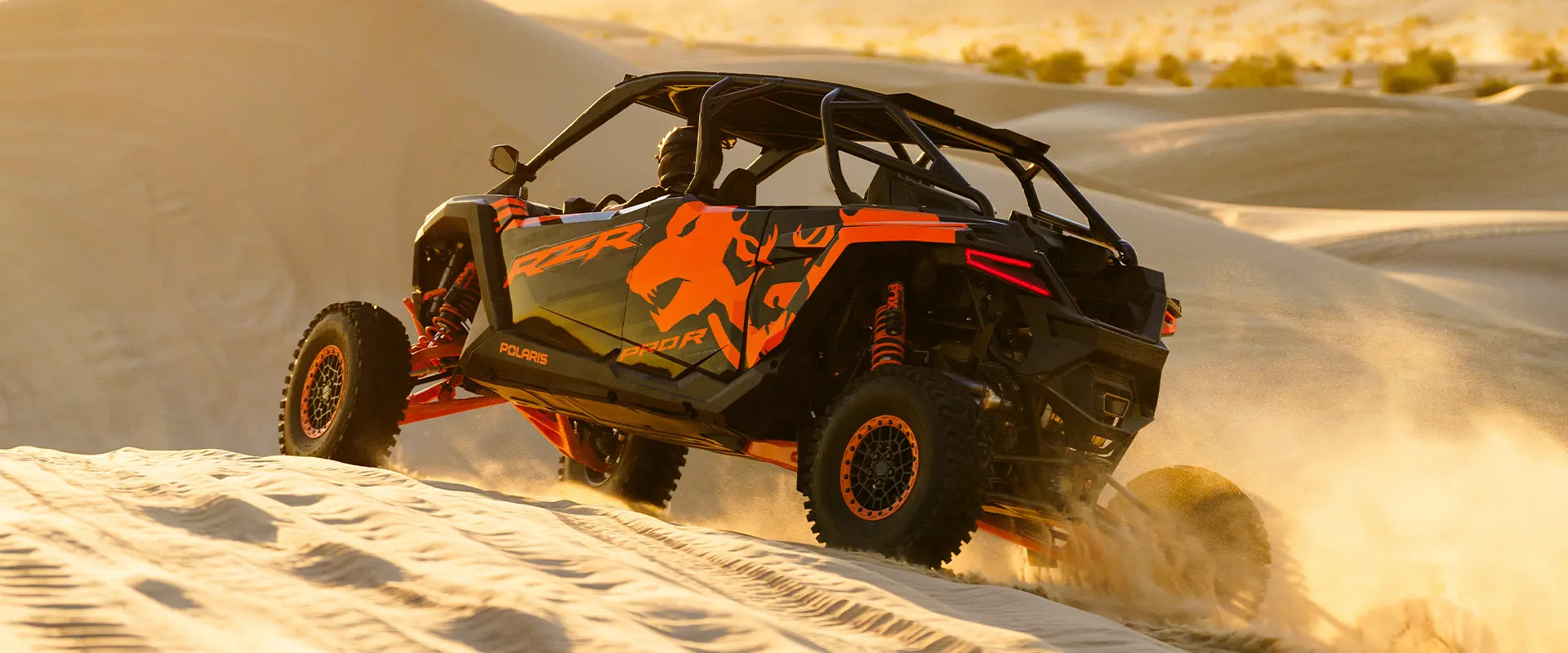 Un VHR côte à côte Polaris RZR Pro R 2025 se déplaçant sur un terrain sablonneux en fin d’après-midi.