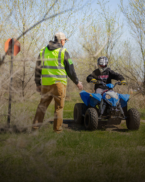 A Polaris youth ATV rider approaches safety instructor outdoors, highlighting safe riding training and gear.