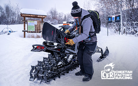 Woman attaching a snowboard to a Polaris snowmobile with a CFR rack at a trailhead.