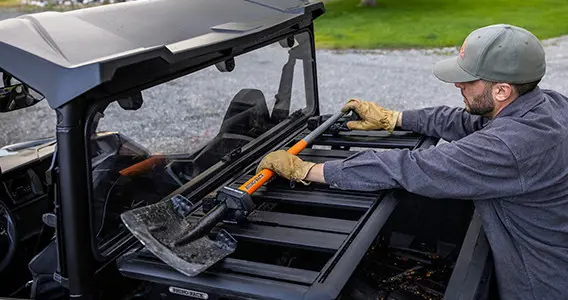 man loading a shovel onto the cargo box on his general xp 1000 side by side