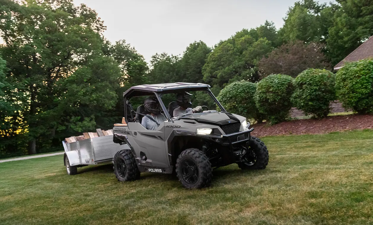 2 people hauling wood in a trailer pulled by their polaris general 1000 side by side