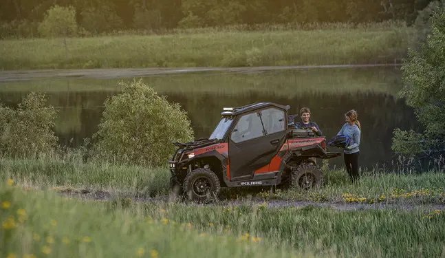 2 people unloading gear from the cargo box on their polaris general 1000 recreational side by side