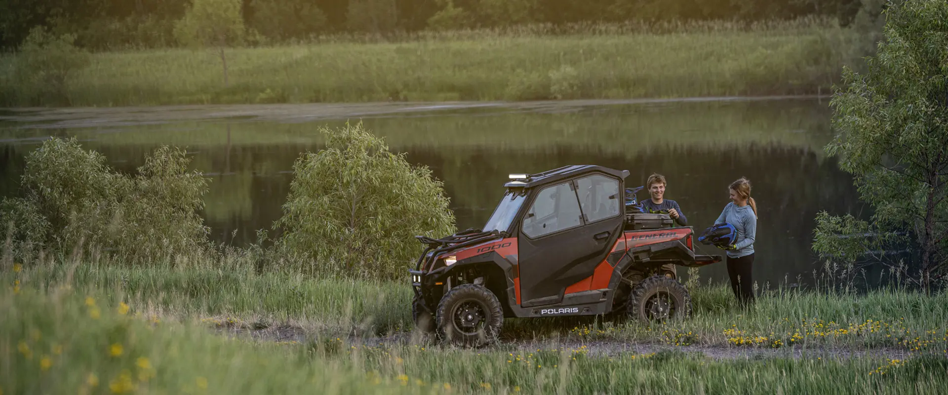 2 people unloading gear from the cargo box on their polaris general 1000 recreational side by side