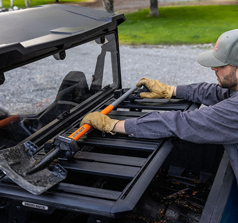 Man placing a shovel in the Lock & Ride accessories in the cargo box of a 2025 GENERAL 1000 side-by-side.