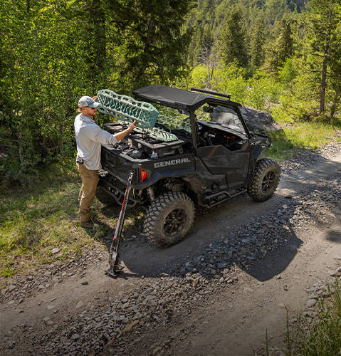 Man loading gear into the versatile cargo box on his 2026 Polaris GENERAL XP 1000 SxS UTV.