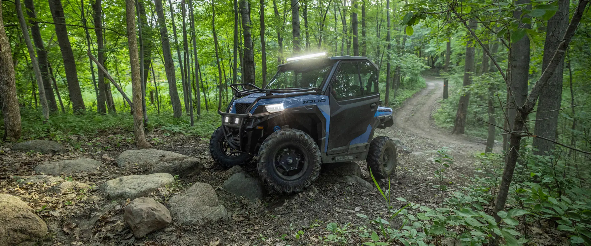 A 2026 Polaris GENERAL crossover side-by-side in the Zenith Blue colorway traversing rocky terrain.