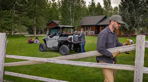 A couple using the cargo box on a 2026 Polaris GENERAL crossover side-by-side to help them install fence.