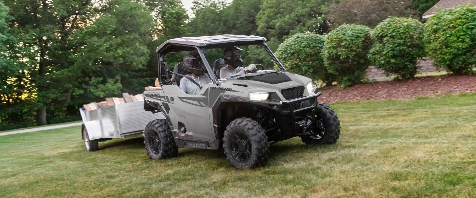 A 2026 Polaris GENERAL crossover side-by-side pulling a trailer through a yard.