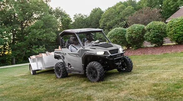 A 2026 Polaris GENERAL crossover side-by-side pulling a trailer through a yard.