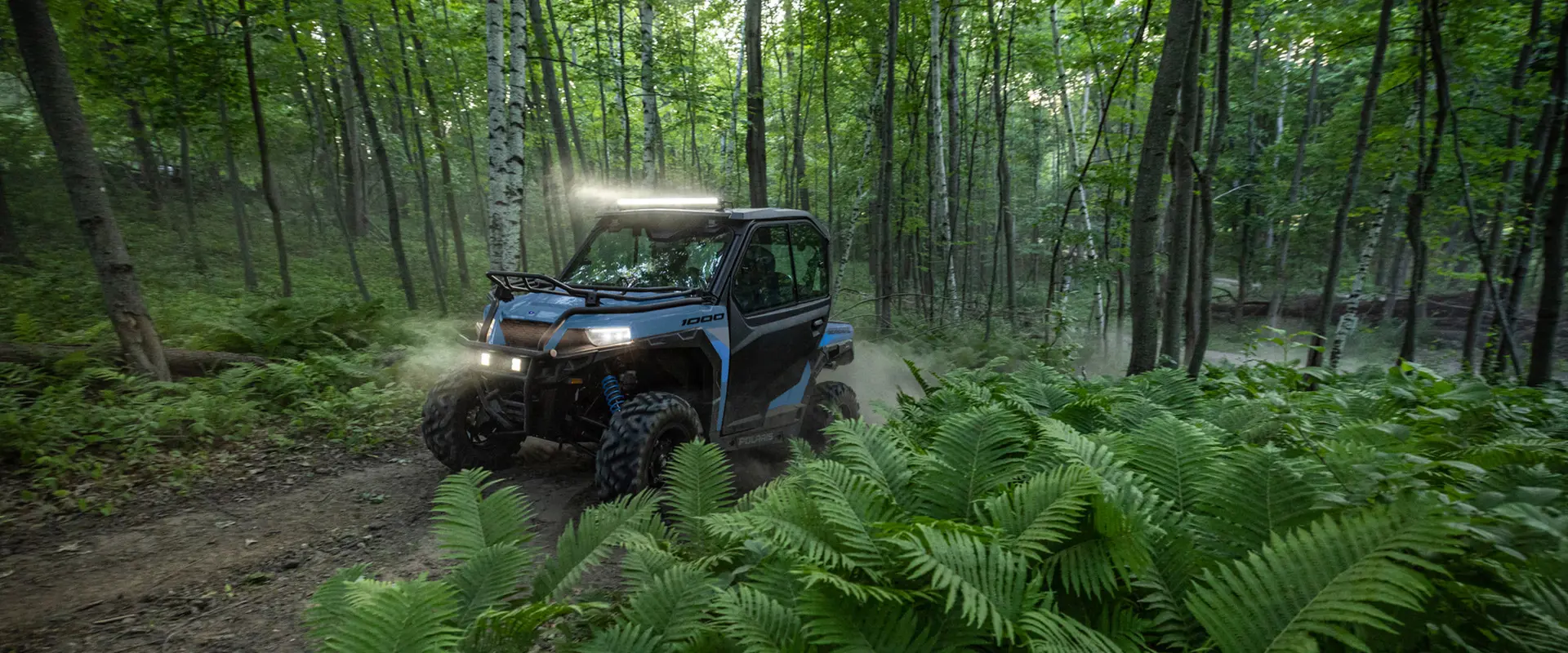 A 2026 Polaris GENERAL crossover side-by-side with a lightbar installed on the roof driving through a forest.