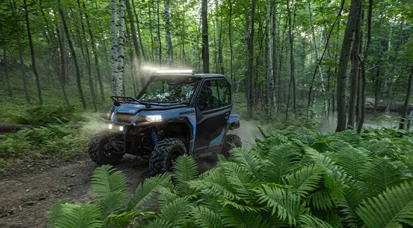 A 2026 Polaris GENERAL crossover side-by-side with a lightbar installed on the roof driving through a forest.
