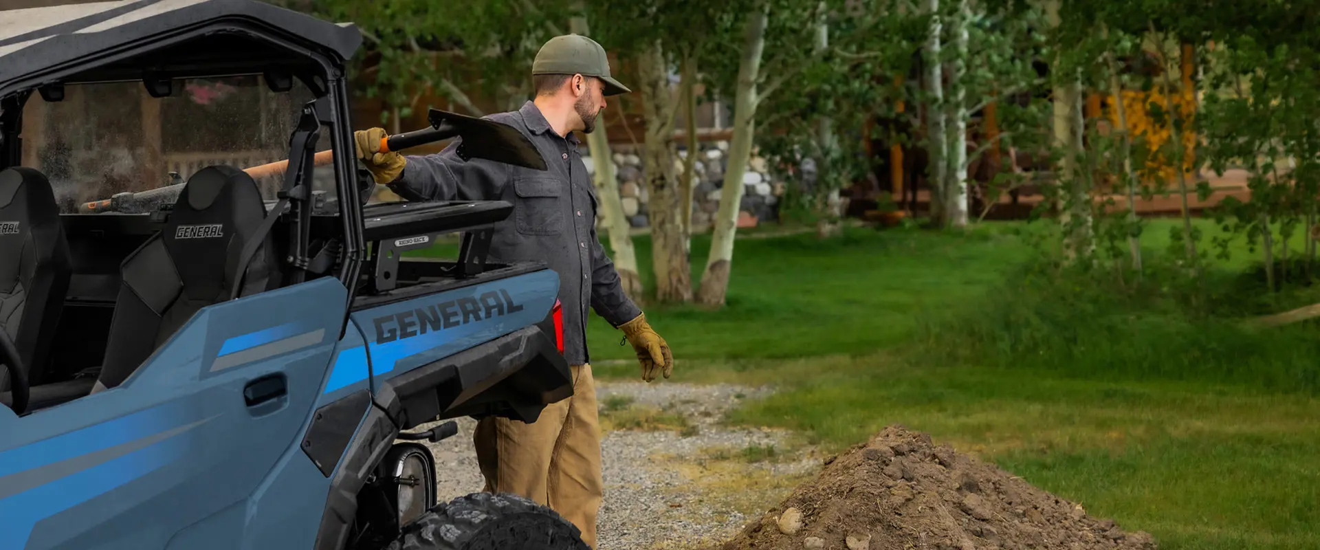 A man grabbing a shovel from the cargo box of his 2026 Polaris GENERAL crossover side-by-side.