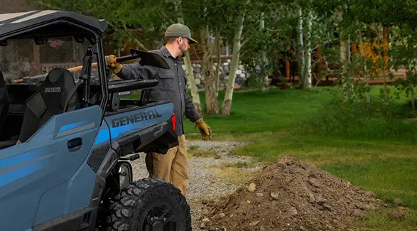 A man grabbing a shovel from the cargo box of his 2026 Polaris GENERAL crossover side-by-side.