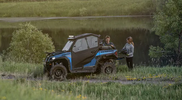 A couple standing by a lake and retrieving items from the cargo box of their 2026 Polaris GENERAL crossover side-by-side.