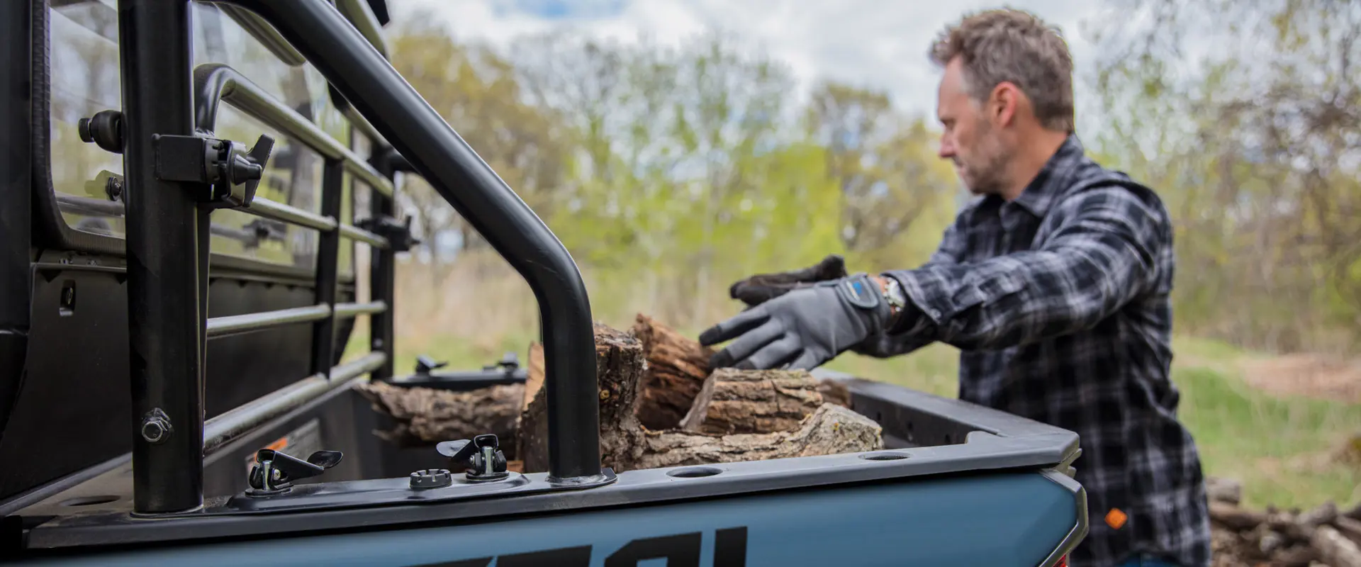 A man loading wood into the cargo box of his 2026 Polaris GENERAL crossover side-by-side.