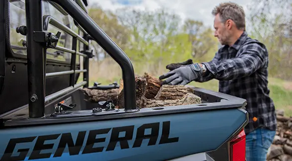 A man loading wood into the cargo box of his 2026 Polaris GENERAL crossover side-by-side.