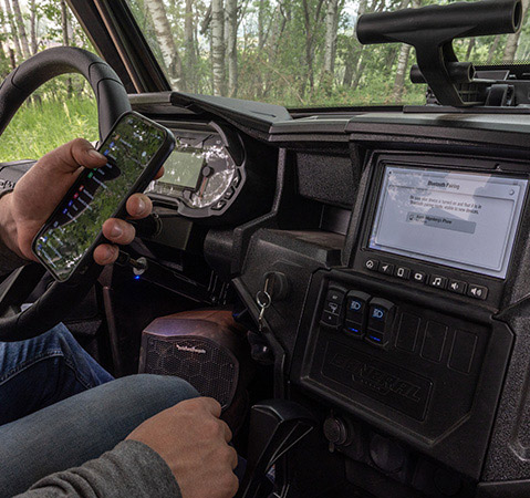 Man connecting his phone to the 7-inch RIDE COMMAND touch screen inside of a 2026 Polaris GENERAL XP 1000 crossover side-by-side.