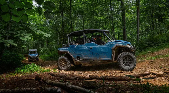 Side profile of a 2026 Polaris GENERAL XP 4 1000 crossover side-by-side cruising through the forest while another GENERAL trails behind.