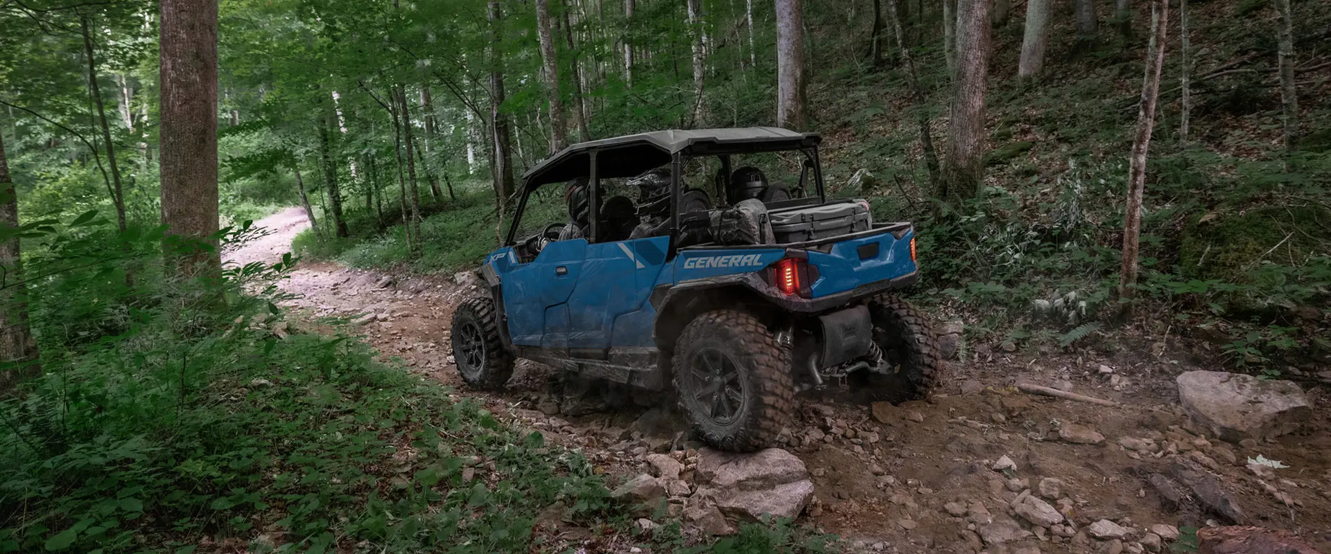 Rear/side view of a 2026 Polaris GENERAL XP 4 1000 crossover side-by-side traversing rocky terrain in a forest.