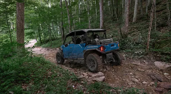 Rear/side view of a 2026 Polaris GENERAL XP 4 1000 crossover side-by-side traversing rocky terrain in a forest.