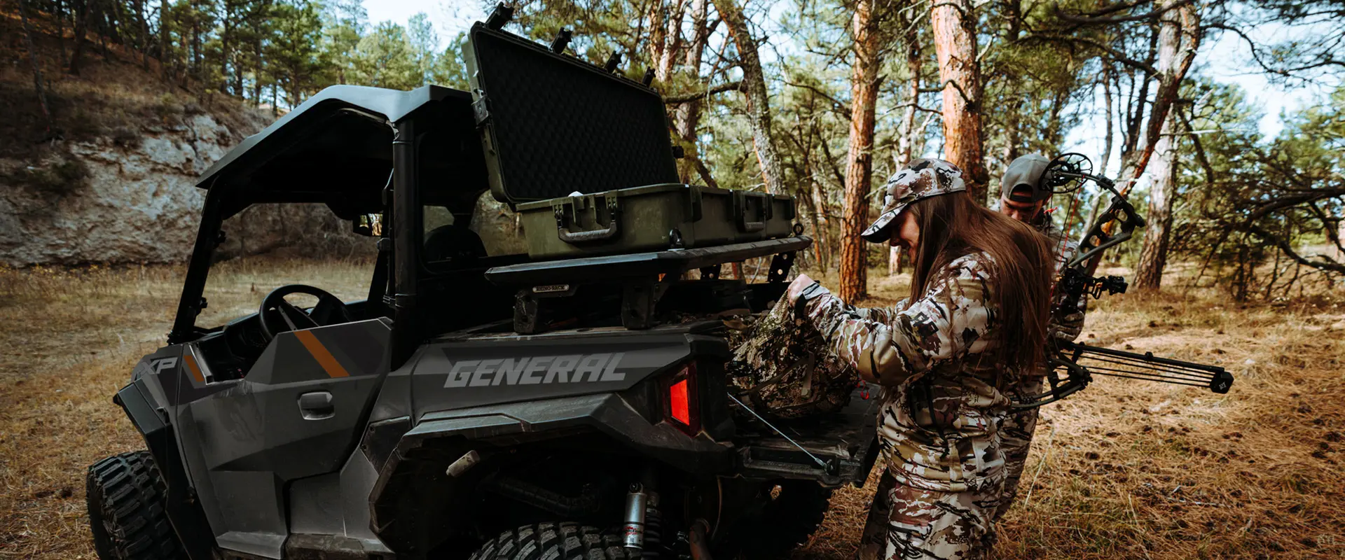 A female hunter grabbing gear from the cargo box of a 2026 Polaris GENERAL XP 1000 crossover side-by-side.