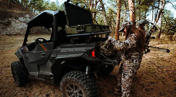 A female hunter grabbing gear from the cargo box of a 2026 Polaris GENERAL XP 1000 crossover side-by-side.