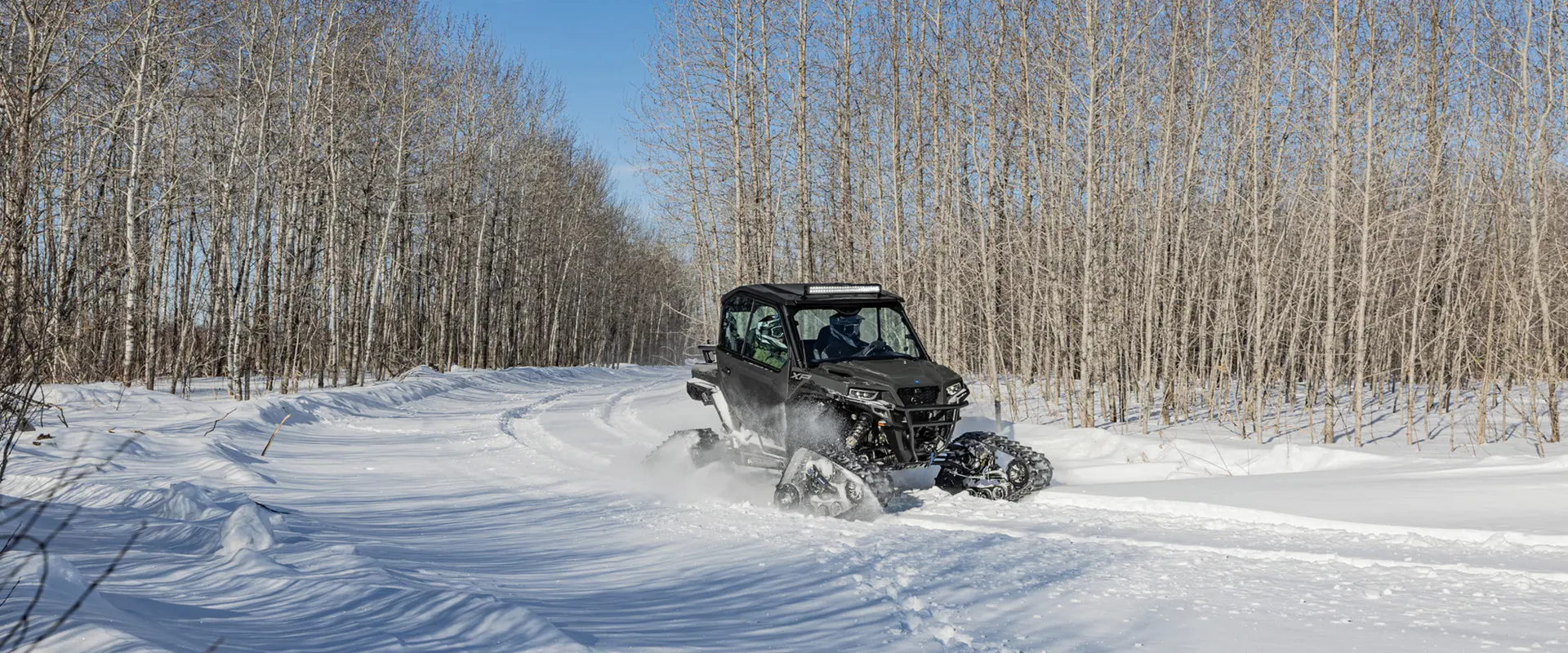 A 2026 Polaris GENERAL XP 1000 crossover side-by-side with tracks installed cruising on a snow-covered trail.